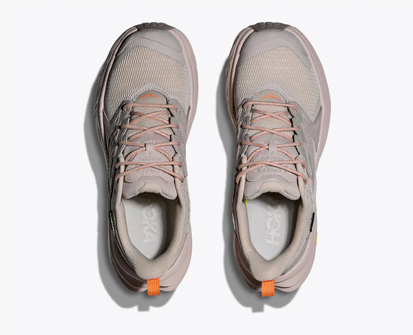Pair of beige running shoes with orange accents on a white background