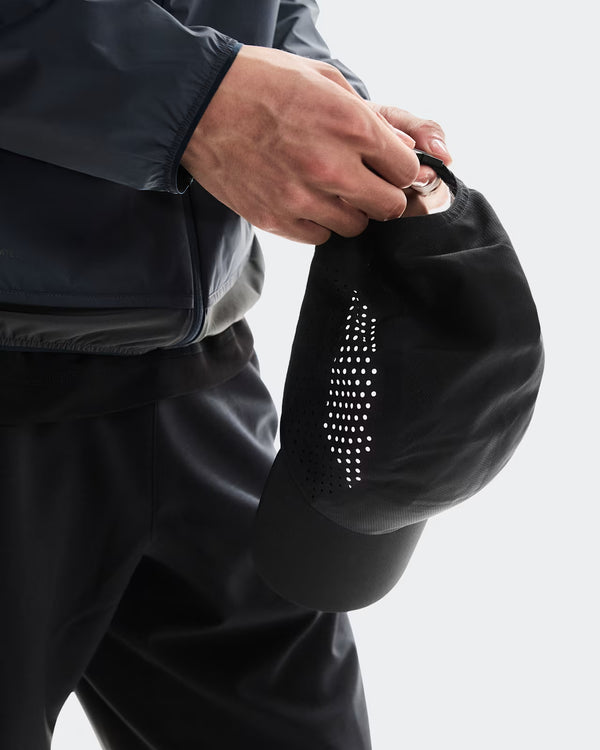 Person holding a black hat with a unique design on a light gray background
