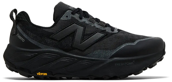 A black New Balance trail running shoe with a dark gray 'N' logo, black laces, and a black Vibram outsole, shown from a side profile on a white background.