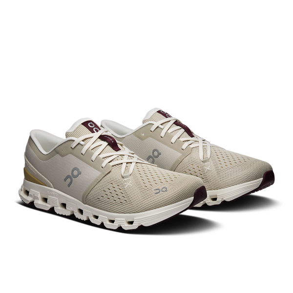 Pair of beige running shoes with white soles on a white background