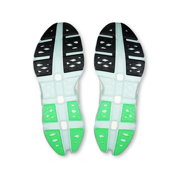 Top-down view of a pair of athletic shoes showing their outsoles, featuring a light mint green base with black tread patterns and bright green accents.