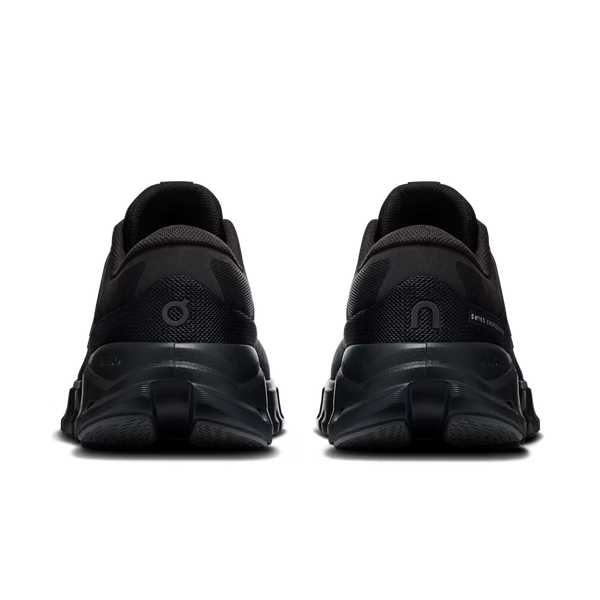 A pair of black athletic sneakers shown from the rear, featuring chunky sculpted black soles and mesh upper panels, set against a plain white background.