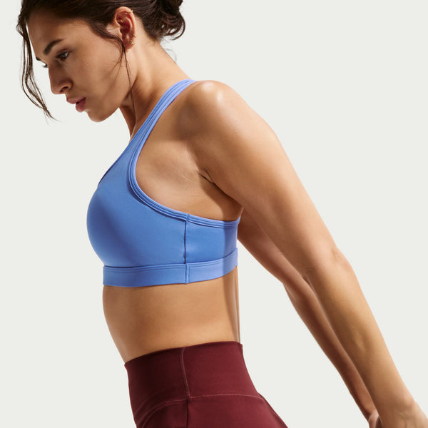 Woman wearing a blue sports bra and maroon leggings on a light gray background