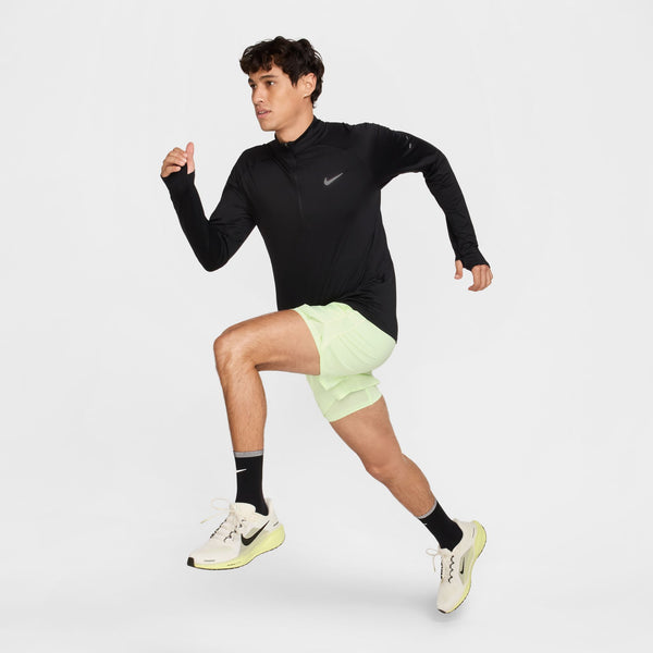 Person wearing a black long-sleeve athletic top and light green shorts on a white background