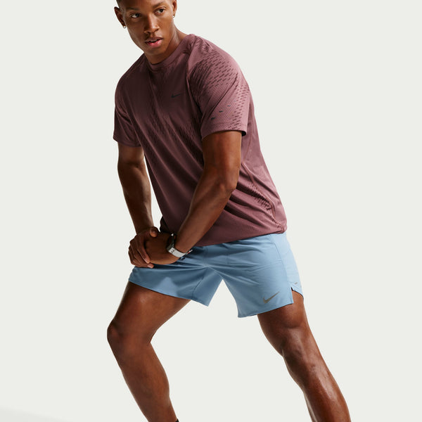 Man wearing a maroon shirt and light blue shorts on a plain background