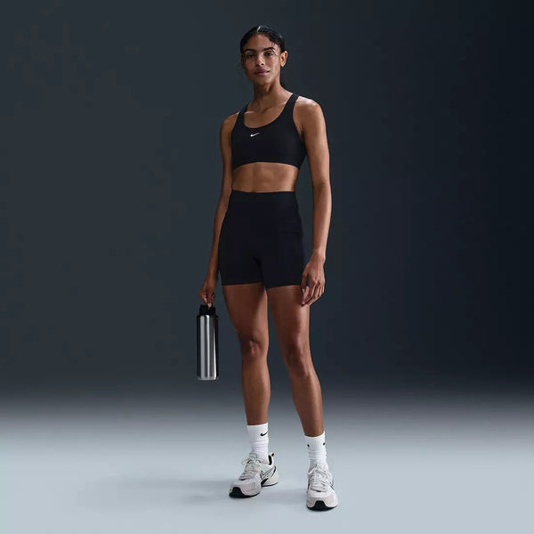 Woman in black Nike athletic wear holding a water bottle against a dark background