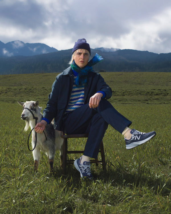This picture is hilarious. It shows a young man wearing 990's sitting in a green grass field with a goat