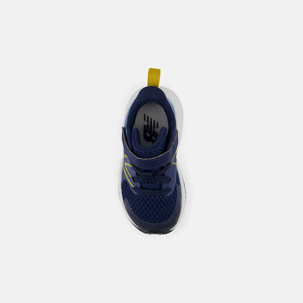 A single New Balance sneaker shown from a top-down view, featuring a navy blue mesh upper, navy hook-and-loop strap, white midsole, and a bright yellow pull tab.
