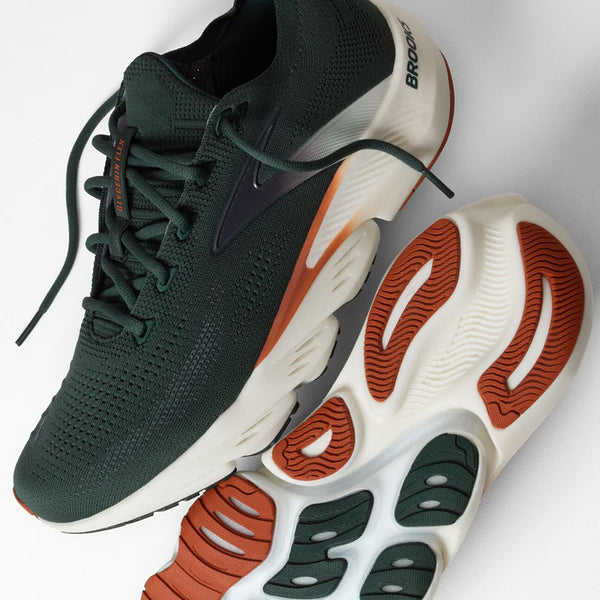 A pair of Brooks running shoes in dark forest green and white, with orange accents on the midsole and outsole, shown on a light gray background.
