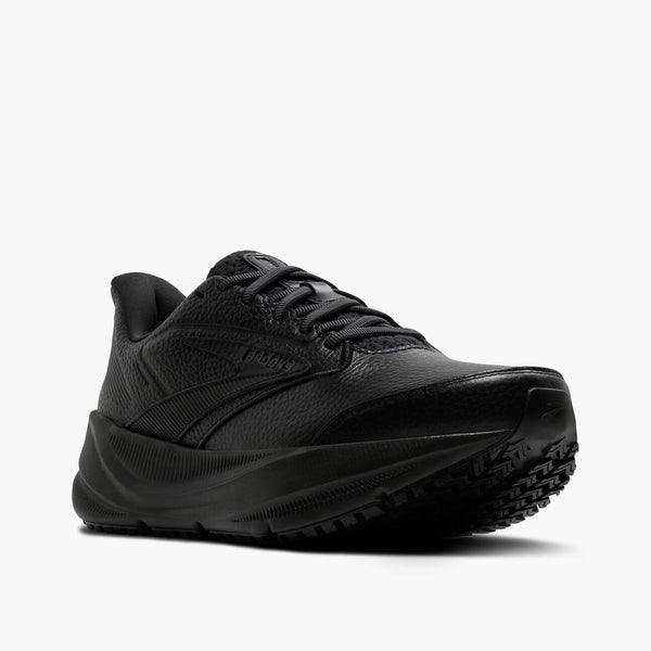 A black low-top athletic shoe with a textured leather upper, matching black laces, and a thick black sole, shown from a three-quarters angle on a light gray background.