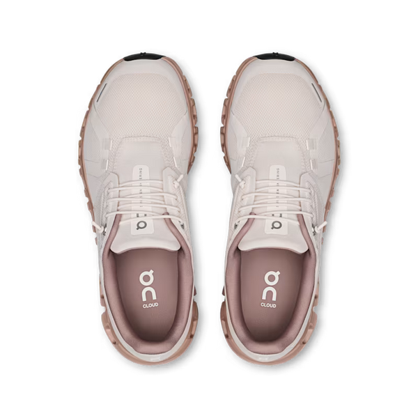 A pair of On Cloud running shoes shown from a top-down view, featuring a light beige and white mesh upper with a dusty rose pink lining and a chunky light brown sole.