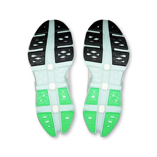 A pair of athletic shoes shown from the sole view, featuring a light mint green and white midsole with bright green cushioned sections and black outsole tread.