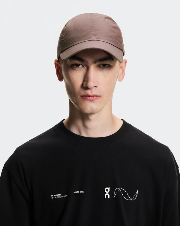 Person wearing a black t-shirt with a logo and a grape colored cap on a white background