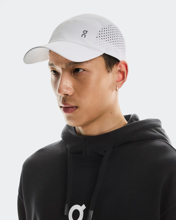 Person wearing a black hoodie and white cap with a logo on a light gray background