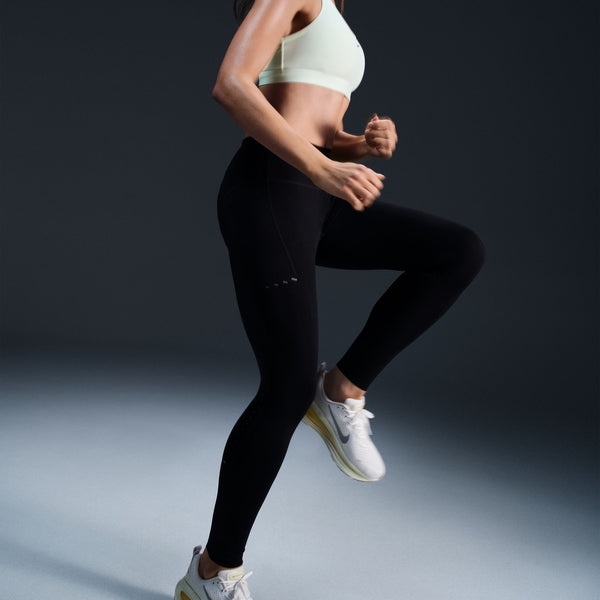 Person running in black leggings and white sneakers on a dark background