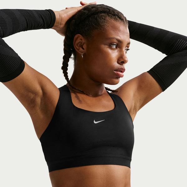 Woman wearing a black Nike sports bra with arms raised against a neutral background