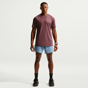 Man wearing a maroon t-shirt and light blue shorts on a white background