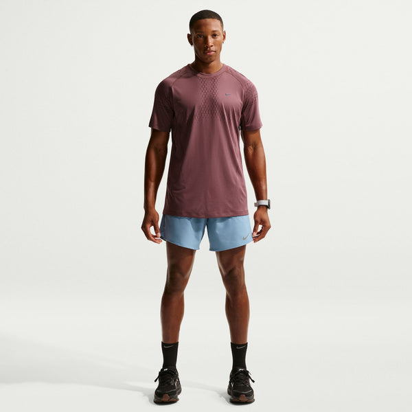 Man wearing a maroon t-shirt and light blue shorts on a white background