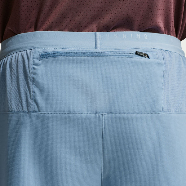 Close-up of blue pants with a zipper pocket, worn with a maroon shirt.