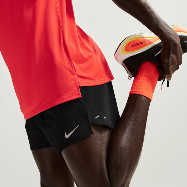 Person wearing red athletic shirt and black shorts with Nike logo, holding a colorful running shoe.
