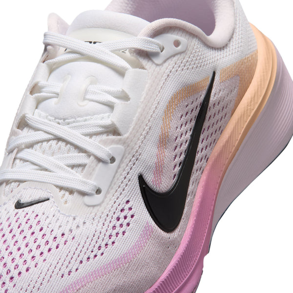 Close-up of a Nike running shoe in white mesh with a black Swoosh, pink and peach gradient accents, and white laces on a white background.