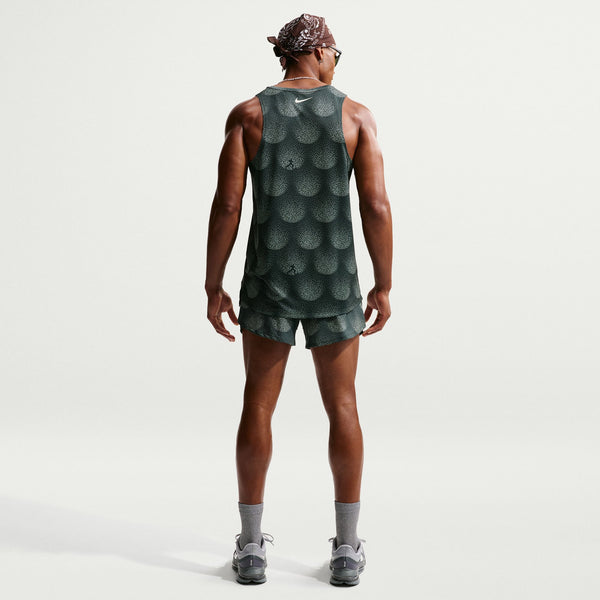 Person wearing a green patterned tank top and shorts on a light gray background