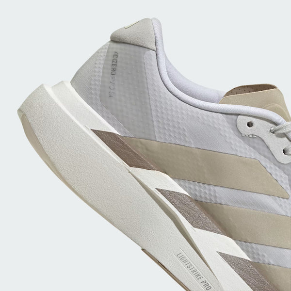 Close-up of a white and beige running shoe showing the side profile, textured mesh upper, thick cushioned sole, and diagonal stripe accents.