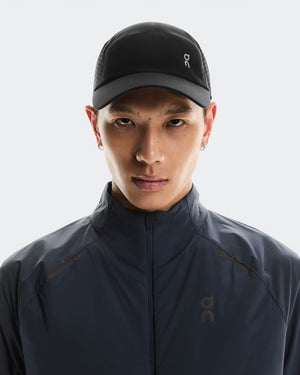 Person wearing a dark jacket and cap with a brand logo on a light gray background