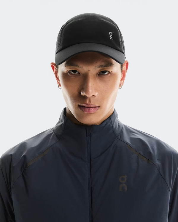 Person wearing a dark jacket and cap with a brand logo on a light gray background