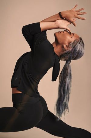 A female in all black side view of her doing a yoga pose with her head back and arms and hands in front of her face.