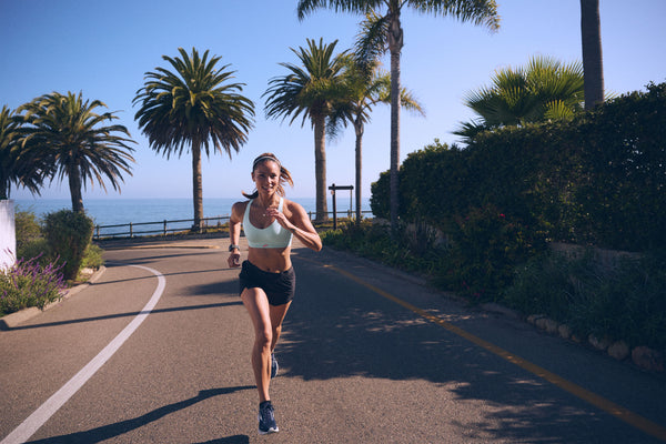 A female runner front view running on a scenic California street with palm trees and the ocean behind her