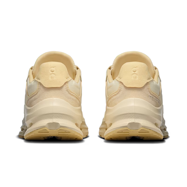 A pair of beige and cream chunky sneakers shown from the back, featuring a thick sculpted sole and a circular logo embossed on the heel tab.