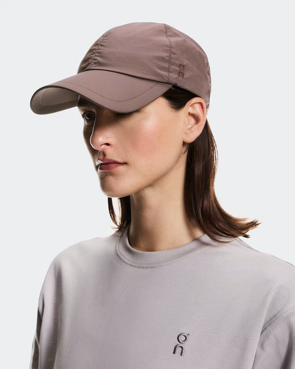 Woman wearing a grape colored cap and gray shirt with a logo on a white background