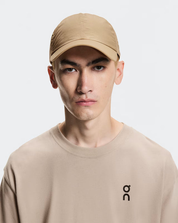 Person wearing a beige cap and matching sweatshirt with a logo on a light gray background