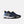 A pair of New Balance athletic sneakers in navy blue with light blue overlays, bright yellow accents on the logo and tongue, and a white midsole, shown against a light gray background.