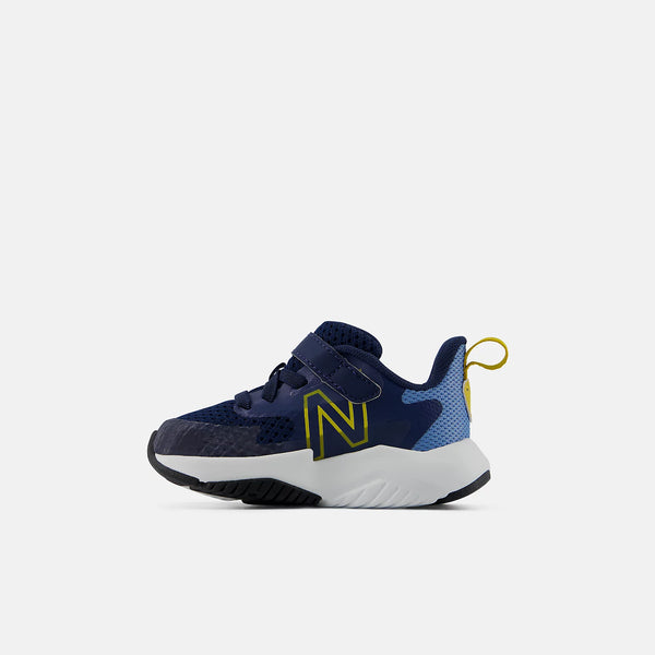 A navy blue New Balance sneaker for kids, featuring a textured navy upper, a light blue mesh heel panel, a prominent yellow 'N' logo, and a thick white midsole.