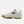 A New Balance tennis shoe in off-white with a black 'N' logo on the side and a brown gum outsole, shown in a side profile view against a light gray background.