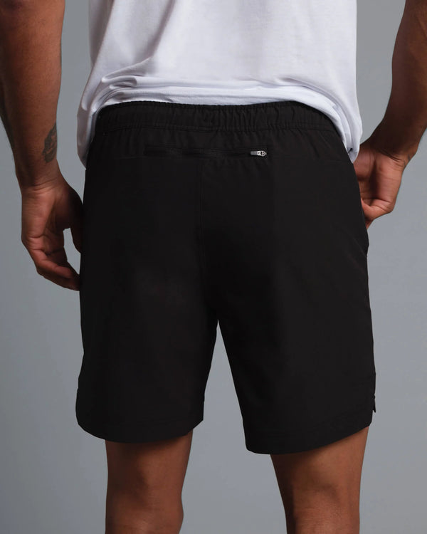 Person wearing black shorts with a small logo on a gray background