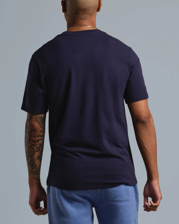 Man wearing a navy blue t-shirt and light blue pants against a gray background