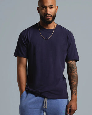 Man wearing a navy blue t-shirt and blue shorts against a gray background
