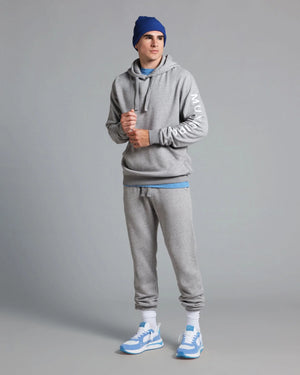Person wearing a gray hoodie and jogger set with blue accents on a gray background