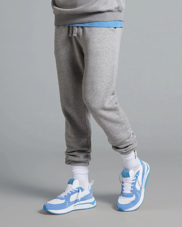 Person wearing gray sweatpants and blue and white sneakers on a gray background