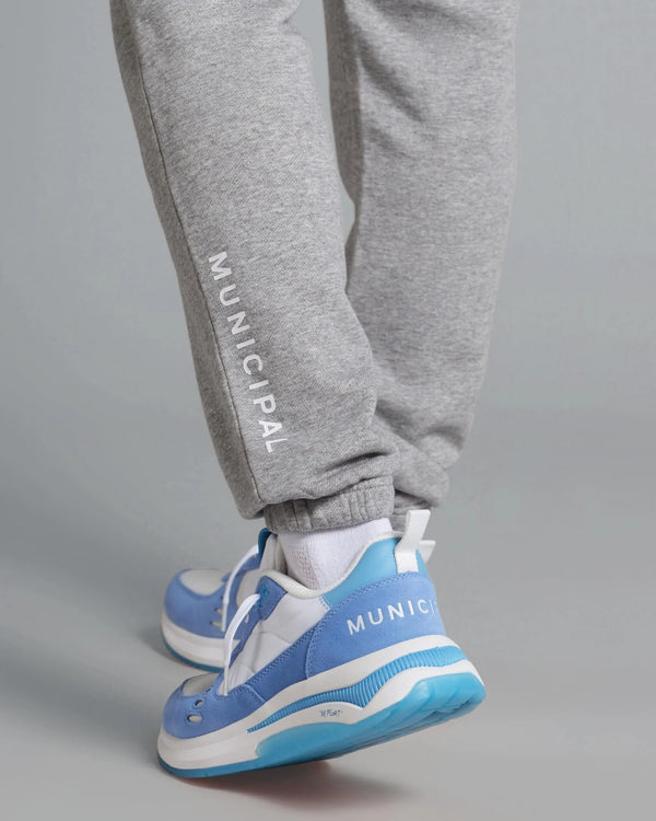 Gray sweatpants with 'Municipal' branding and blue sneakers on a gray background