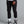 Person wearing black jogger pants and black and white sneakers on a gray background