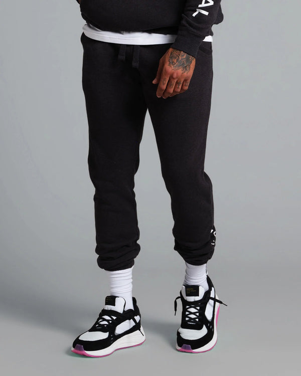 Person wearing black jogger pants and black and white sneakers on a gray background