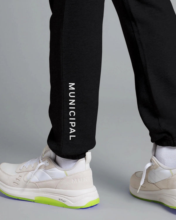Black pants with 'MUNICIPAL' text worn by a person on a gray background