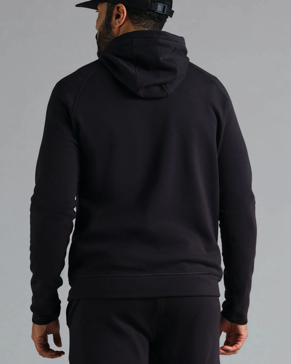 Person wearing a black hoodie and pants on a gray background