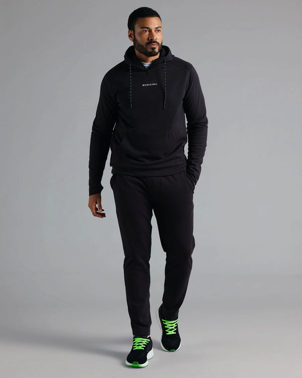 Man wearing a black hoodie and pants with green accents on a gray background