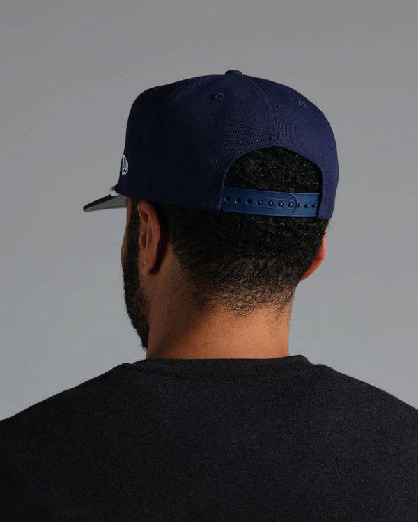 Person wearing a navy blue cap with a logo on the back against a gray background