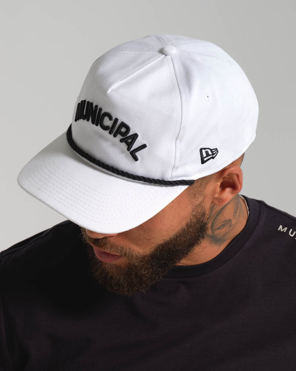 Man wearing a white cap with 'Municipal' text and a black t-shirt on a gray background.